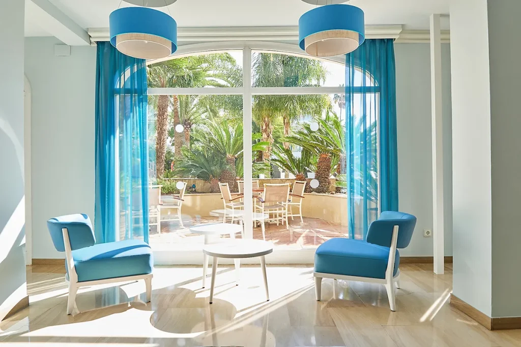 Sala luminosa con sillas azules frente a una ventana y vistas al jard&iacute;n.