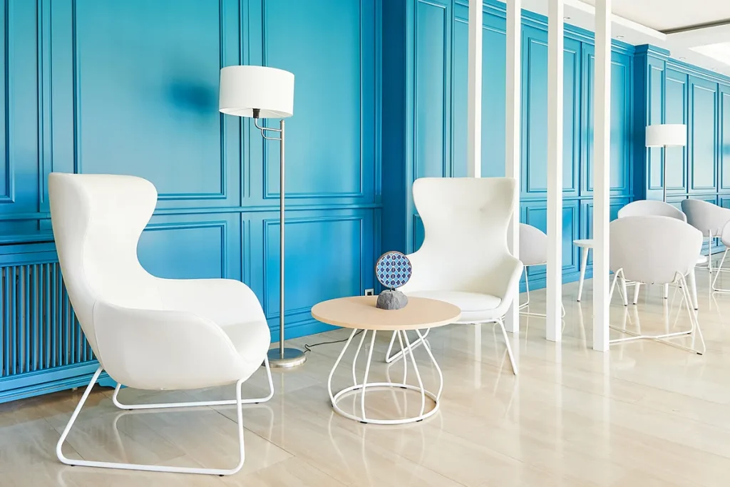 Sala con sillones blancos, pared azul y luz natural.