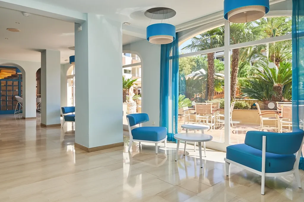 Sala luminosa con muebles azules y vista a un jard&iacute;n con palmeras.
