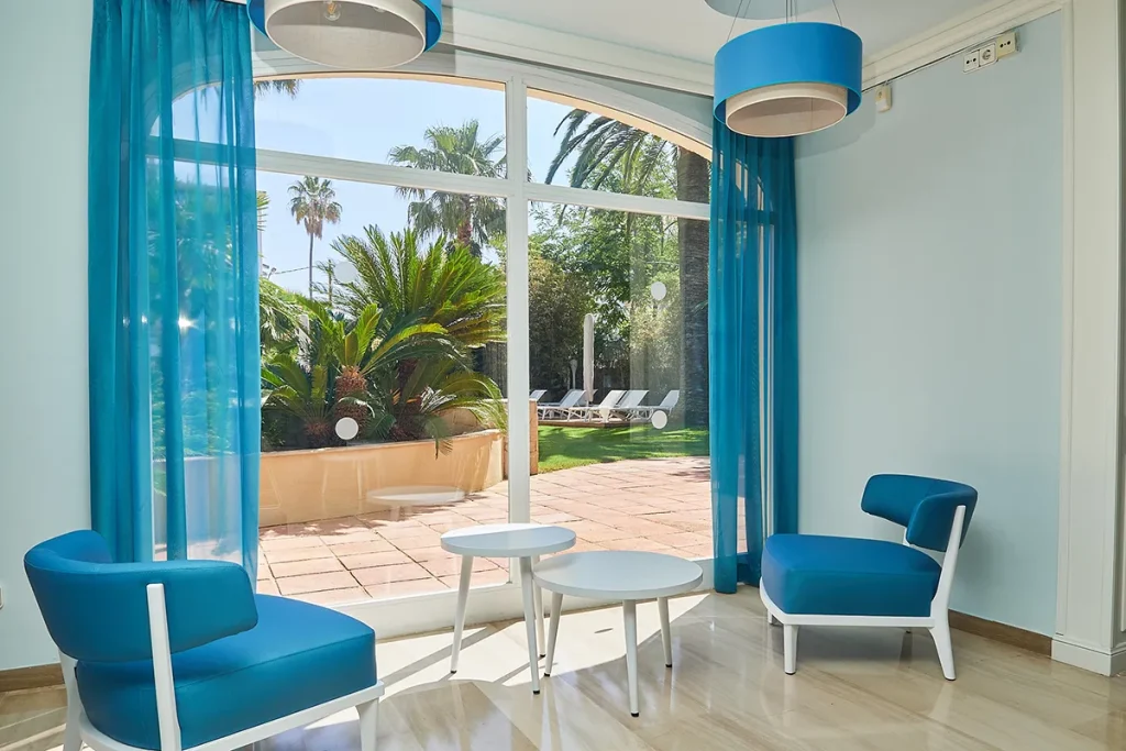 Sala con sillas azules y vista al jard&iacute;n tras puertas de cristal.