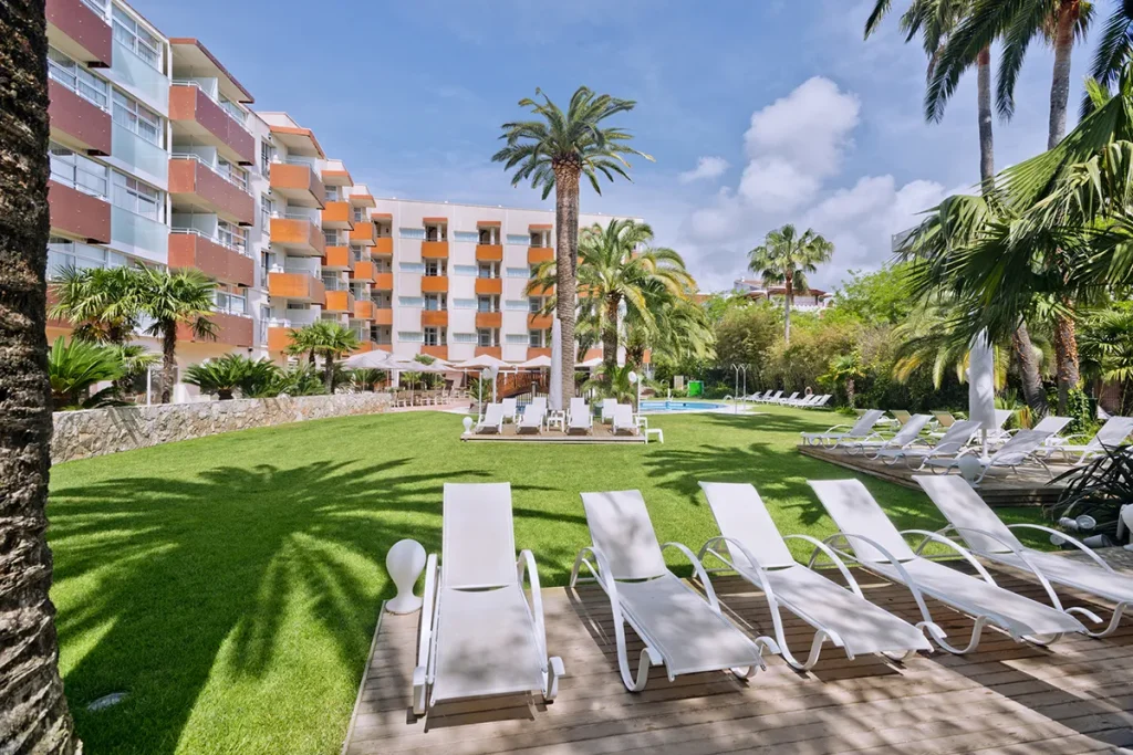 Edificio moderno con jard&iacute;n, palmeras y tumbonas al sol.