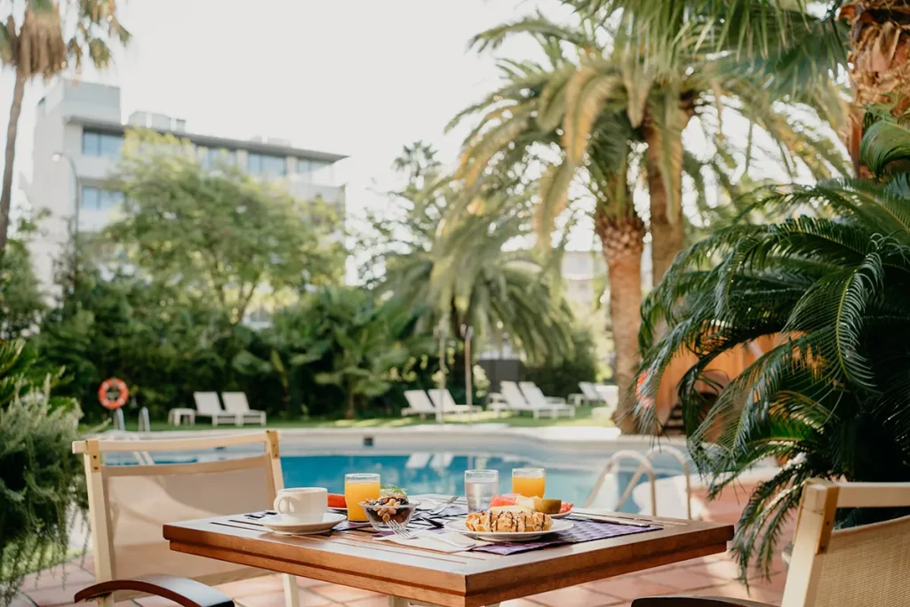 Desayuno al aire libre junto a una piscina con palmeras alrededor.