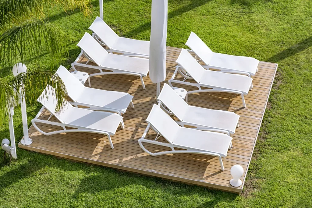Tumbonas blancas sobre plataforma de madera rodeada de c&eacute;sped verde.