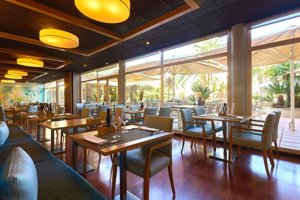 Restaurante moderno con sillas azules y mesas de madera junto a ventanas grandes.