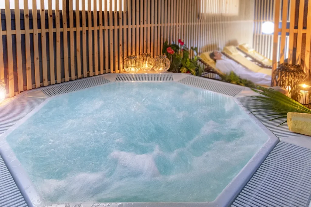 Jacuzzi en spa con luces c&aacute;lidas y tumbonas de relajaci&oacute;n al fondo.