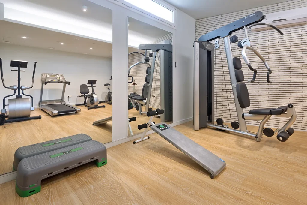 Gimnasio con m&aacute;quinas de ejercicio y espejos en un sal&oacute;n moderno.