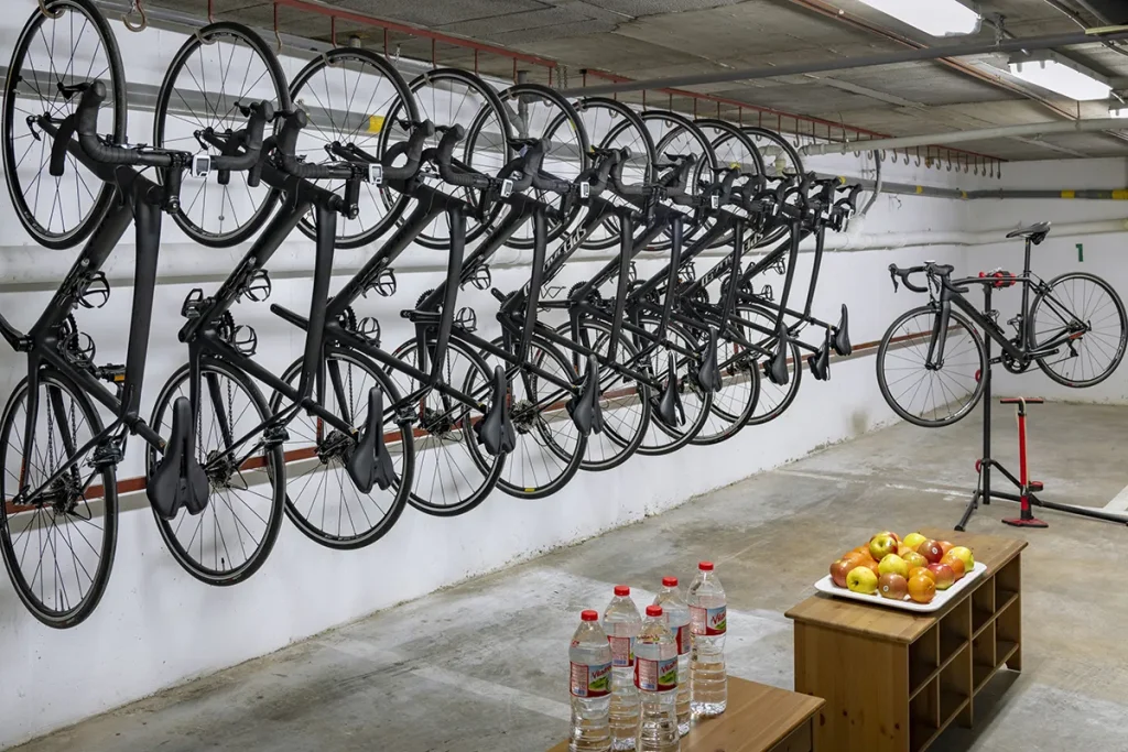 Bicicletas colgadas, mesa con frutas y botellas de agua en un estacionamiento.