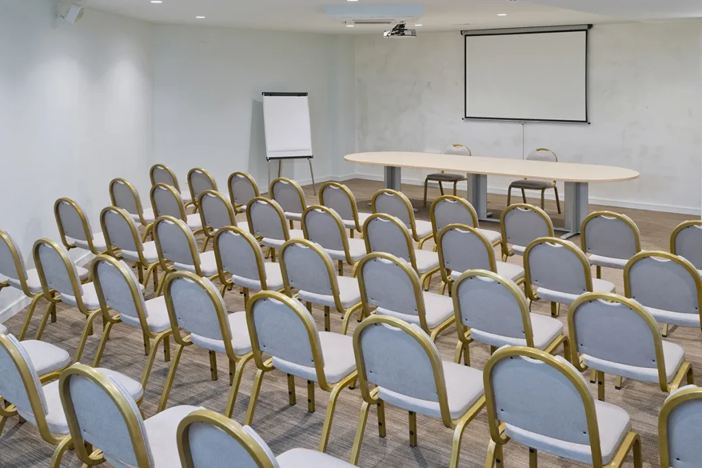 Sala de conferencias con sillas, pantalla y pizarra.