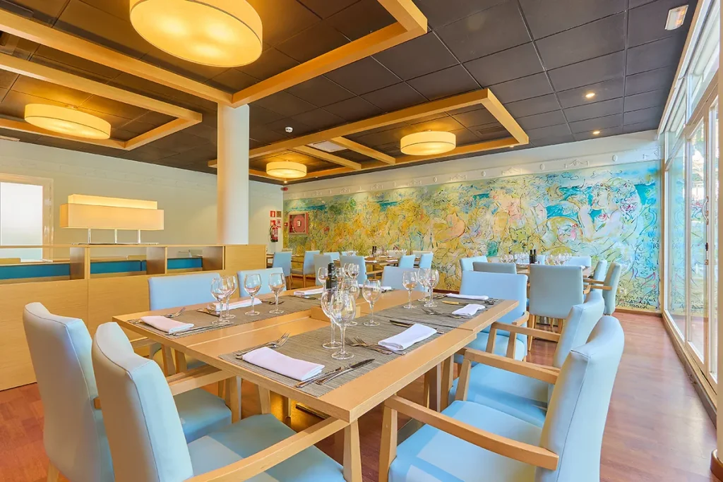 Restaurante elegante con sillas azules y colorido mural en la pared.