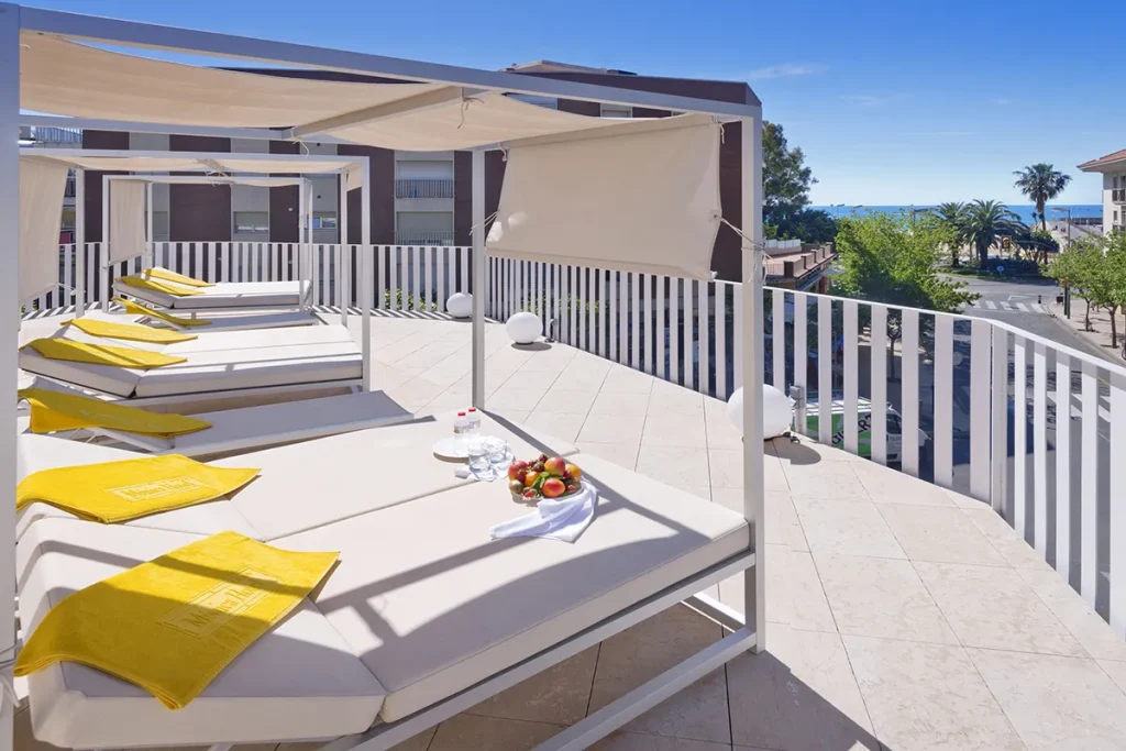 Terraza con camas y vistas al mar, toallas amarillas y fruta sobre la mesa.