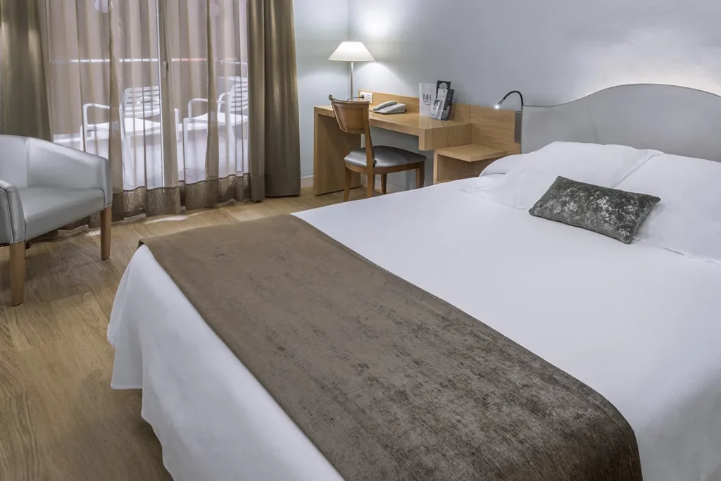 Habitaci&oacute;n de hotel con cama, escritorio y ventana.