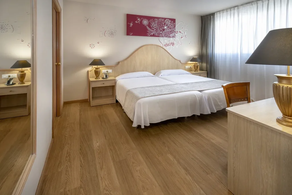 Habitaci&oacute;n de hotel con dos camas, decoraci&oacute;n simple y l&aacute;mparas en bur&oacute;s.