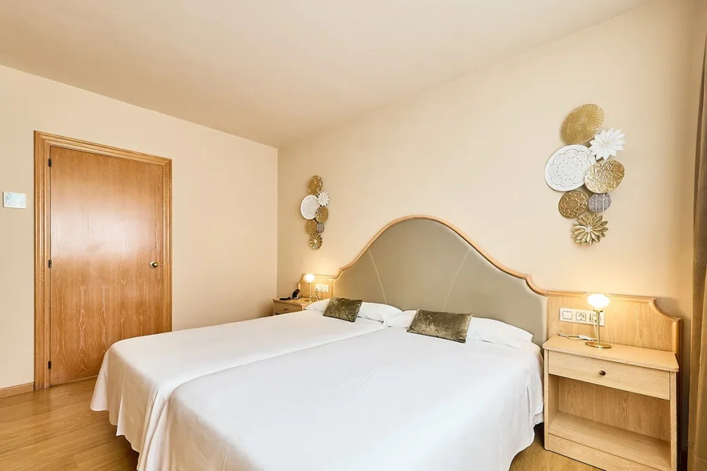 Habitaci&oacute;n con camas gemelas, cabecero curvo y decoraci&oacute;n de pared floral.