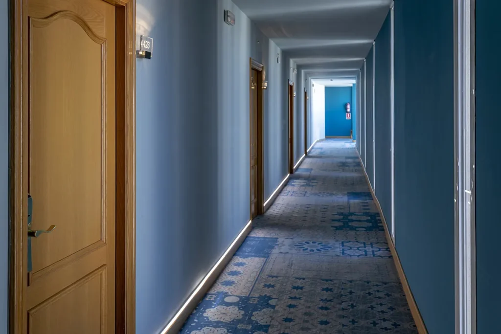 Pasillo de hotel con paredes y puertas numeradas en tono azul claro.