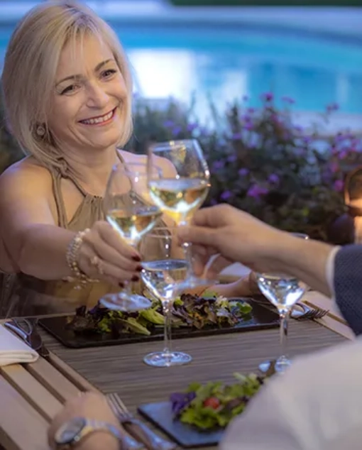 Personas brindando en una cena junto a una piscina.