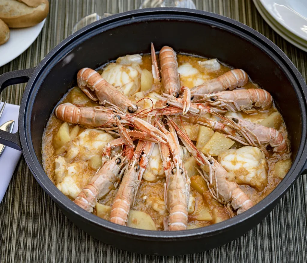 Cazuela de mariscos con cigalas y guiso de papas, servida en una olla negra.