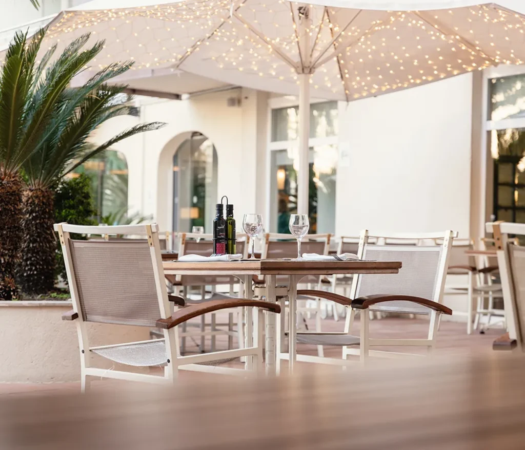 Terraza de restaurante con mesas, sillas y luces en sombrilla.