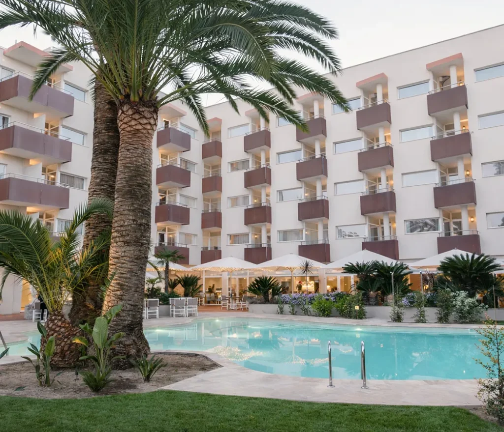 Hotel con piscina y palmeras en un jard&iacute;n.