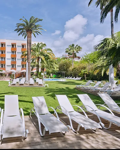 Sillas blancas al aire libre en un hotel con palmeras y c&eacute;sped.