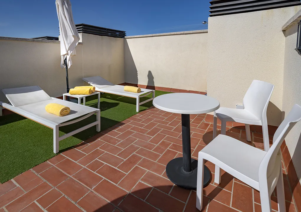 Terraza con tumbonas, toallas amarillas, mesa y sillas blancas bajo el sol.