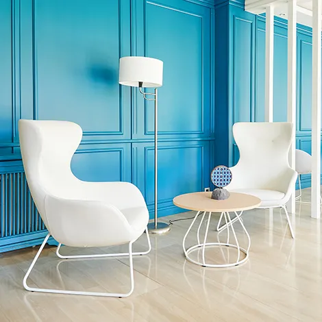 Dos sillones blancos, mesa y l&aacute;mpara en habitaci&oacute;n con pared azul.