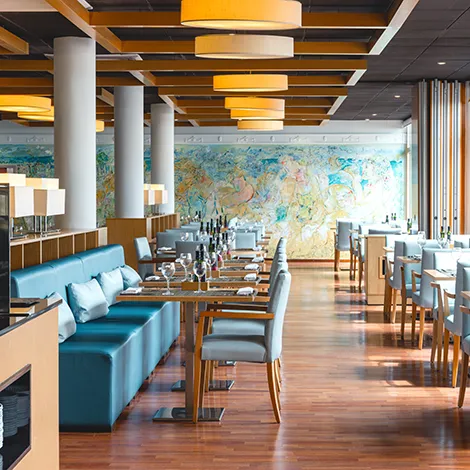 Restaurante elegante con mesas dispuestas, decoraci&oacute;n de madera y mural colorido.