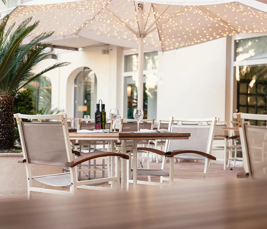 Terraza con mesas, sillas, luces en sombrillas y copas de cristal.