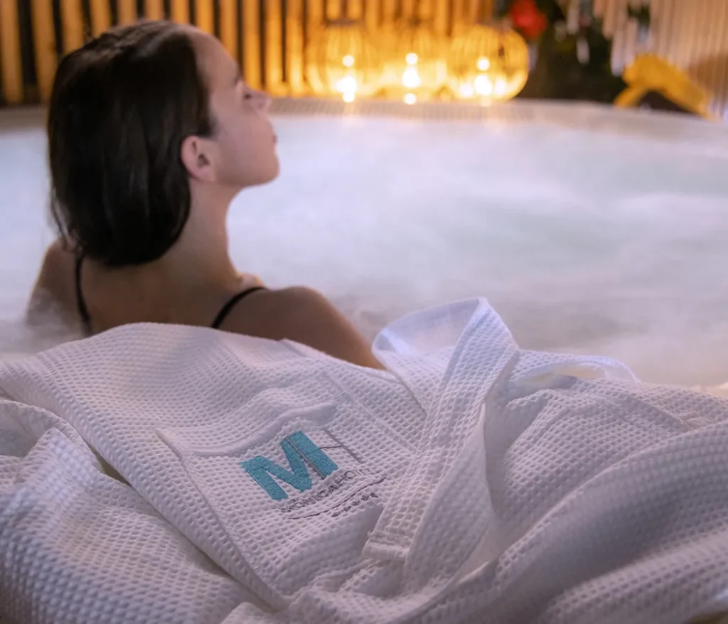 Persona relaj&aacute;ndose en un jacuzzi, con una bata blanca al frente.