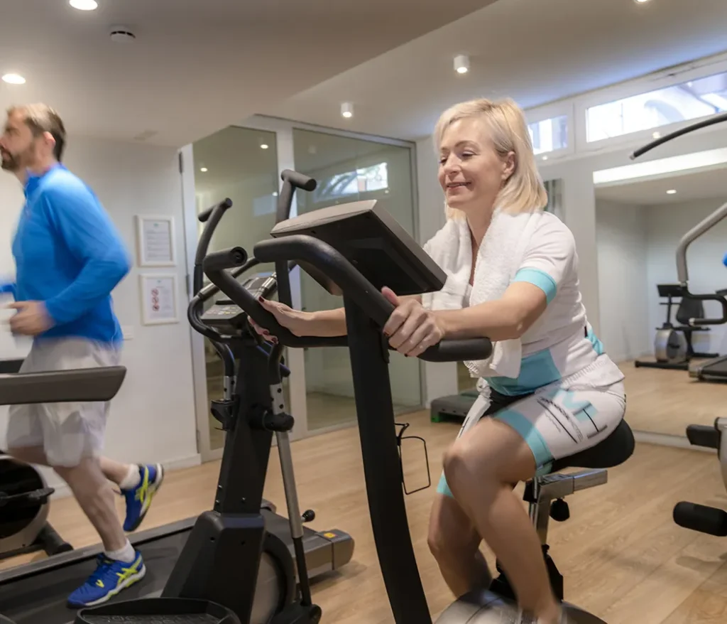 Mujer en bicicleta est&aacute;tica y hombre corriendo en cinta en un gimnasio.