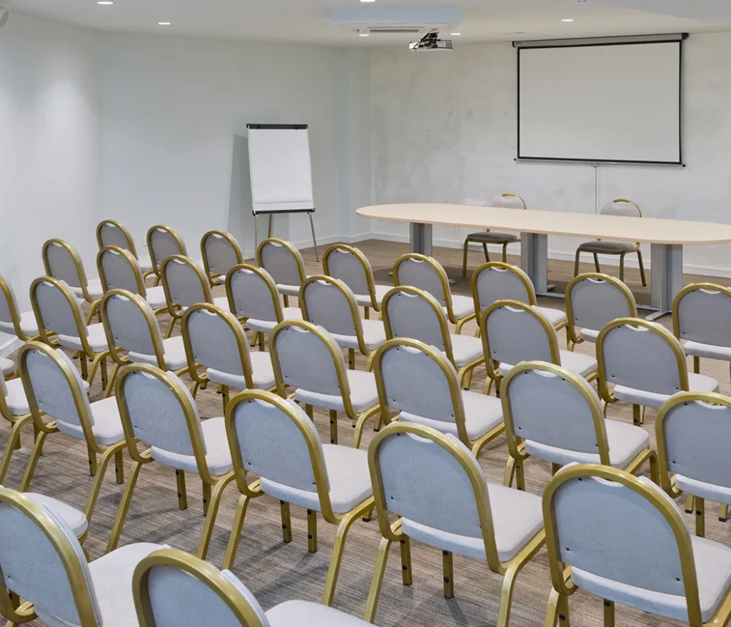 Sala de conferencias vac&iacute;a con sillas, proyector y pantalla.