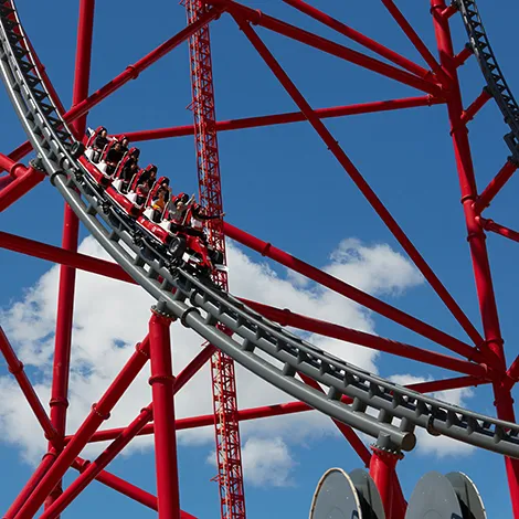 Monta&ntilde;a rusa roja con personas y cielo azul de fondo.