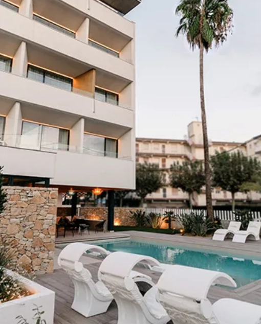 Edificio moderno con piscina, tumbonas y palmera al atardecer.