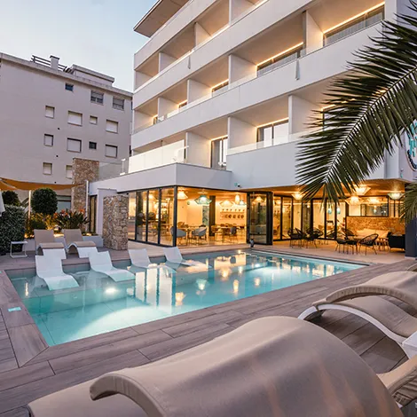 Hotel con piscina iluminada al atardecer y tumbonas modernas.