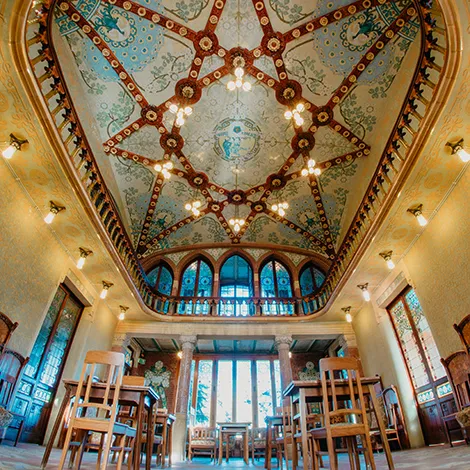 Sala con techo decorado, l&aacute;mparas colgantes y mesas de madera.