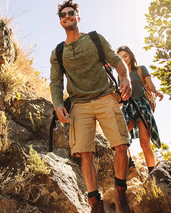 Dos personas caminando por un sendero rocoso al aire libre, bajo el sol.