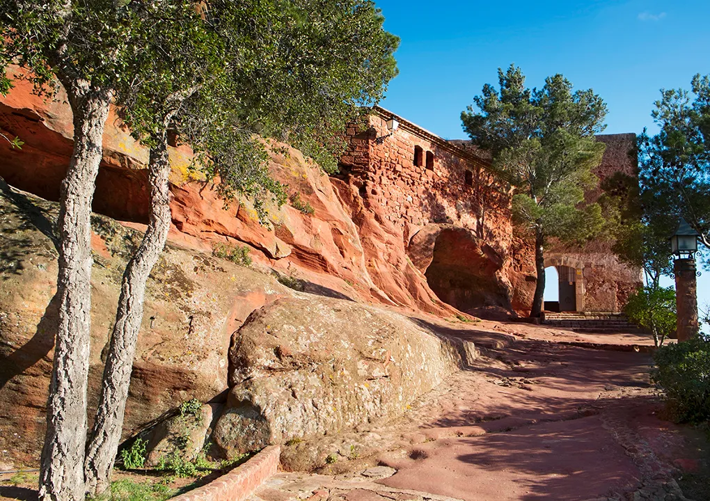 Edificio de piedra rojiza entre &aacute;rboles y cielo azul brillante.