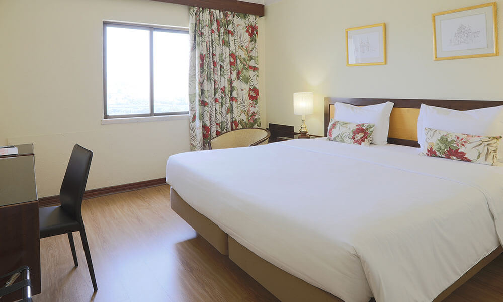 Quarto de hotel com cama de casal, janela e cortinas floridas.