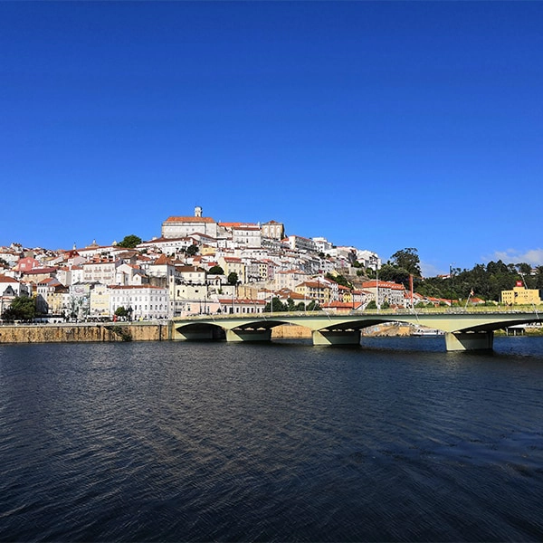 Cidade hist&oacute;rica &agrave; beira do rio sob c&eacute;u azul claro.
