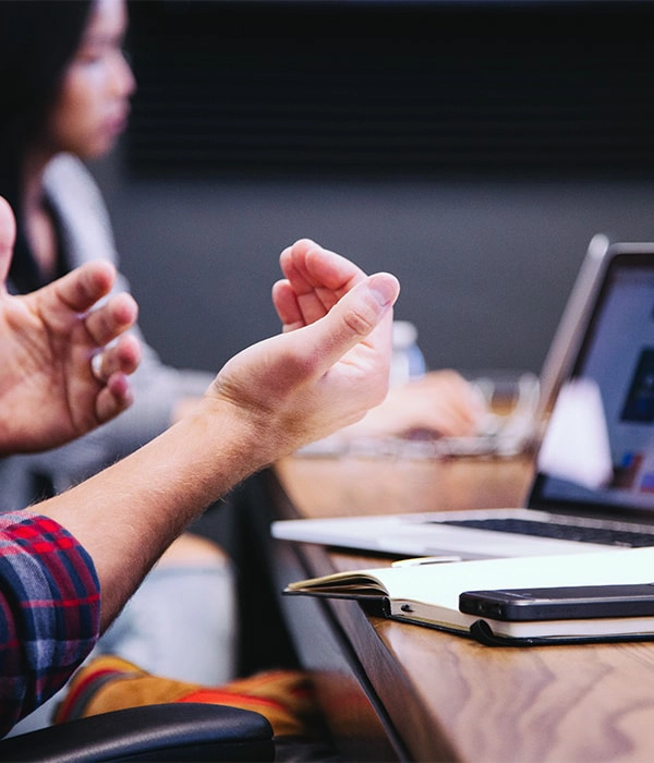 Pessoa gesticulando durante uma reuni&atilde;o em frente a um laptop.