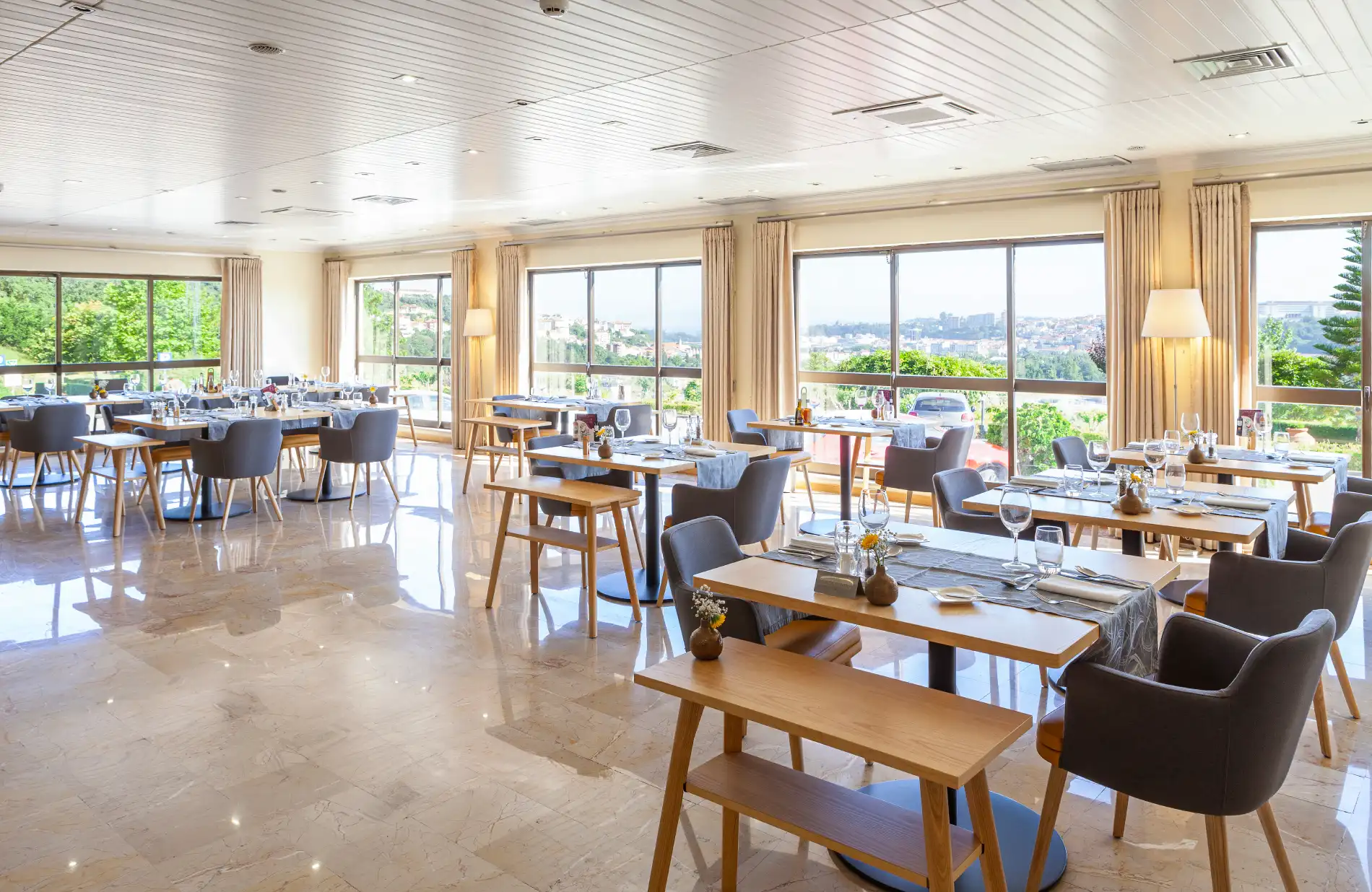 Restaurante moderno e bem iluminado com mesas preparadas e vista externa.