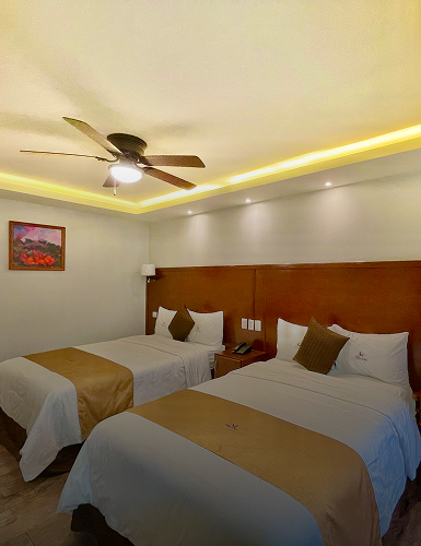 Habitaci&oacute;n de hotel con dos camas dobles, l&aacute;mpara de techo y pintura en la pared.
