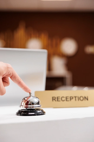 Persona tocando una campana de recepci&oacute;n junto a un cartel que dice "Reception".