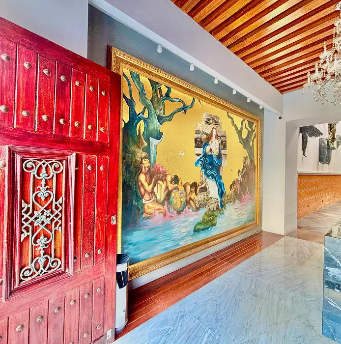 Entrada con puerta roja, mural colorido y techo de madera.