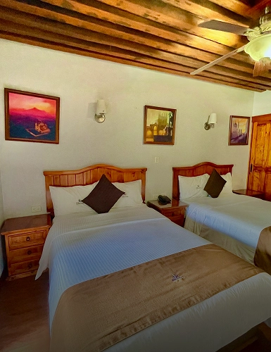 Habitaci&oacute;n con dos camas, l&aacute;mparas de pared y cuadros decorativos.