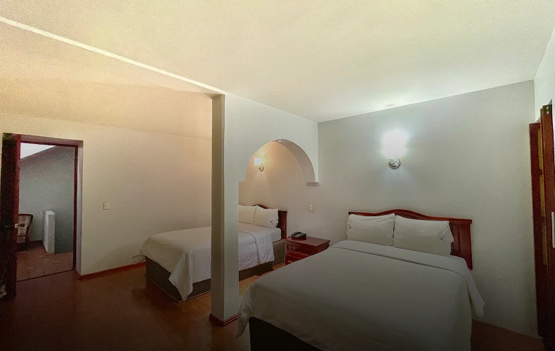 Habitaci&oacute;n con dos camas dobles, paredes blancas y l&aacute;mparas en la pared.