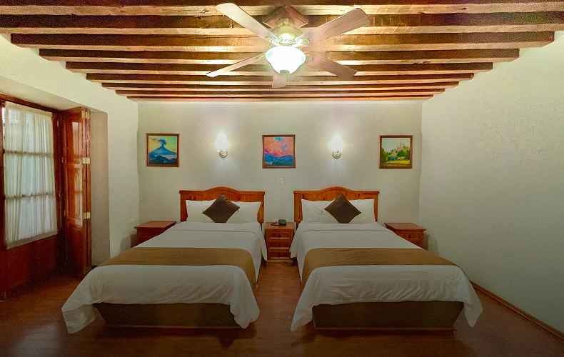 Habitaci&oacute;n con dos camas, techo con vigas y ventilador de techo.