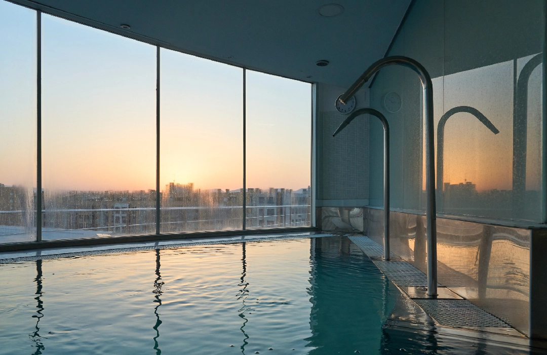 Piscina cubierta con vista al atardecer por grandes ventanales.