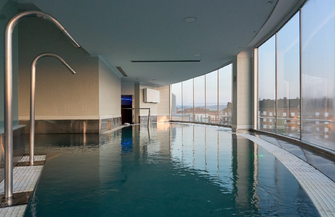 Piscina interior con vista panorámica a la ciudad a través de ventanales.