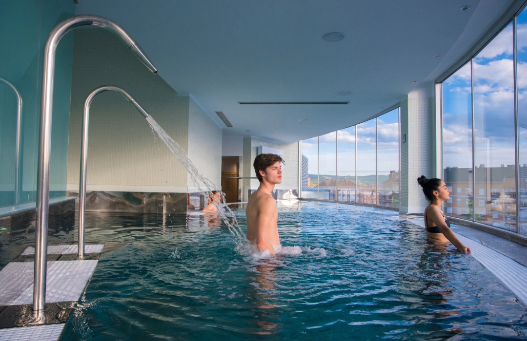 Personas relajándose en una piscina interior con vista panorámica.