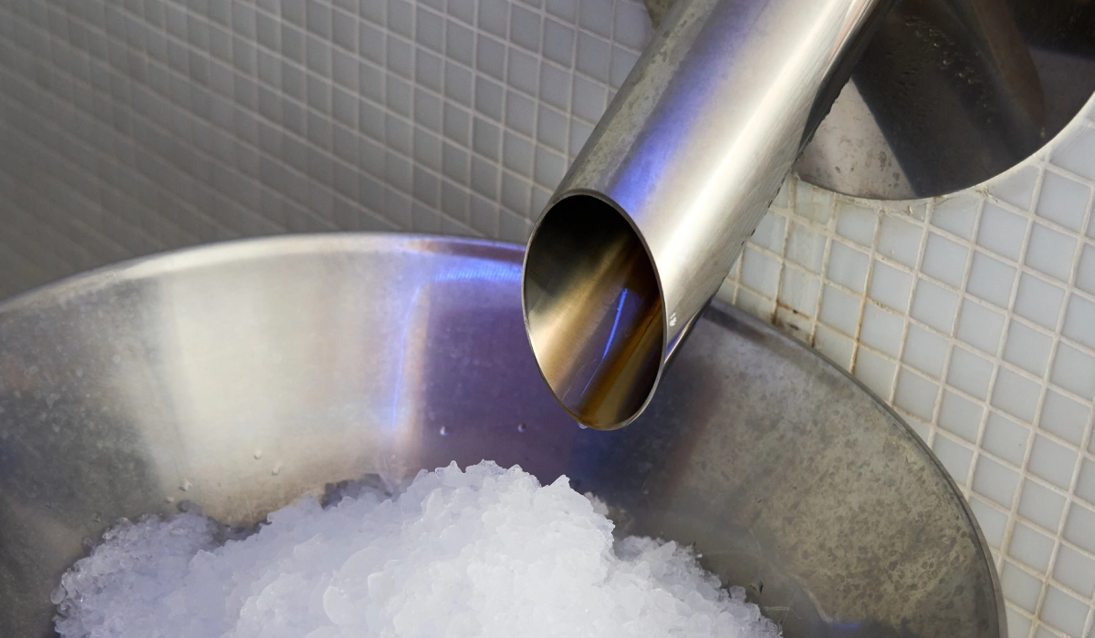 Tubo de metal vertiendo l&iacute;quido a un recipiente con hielo.